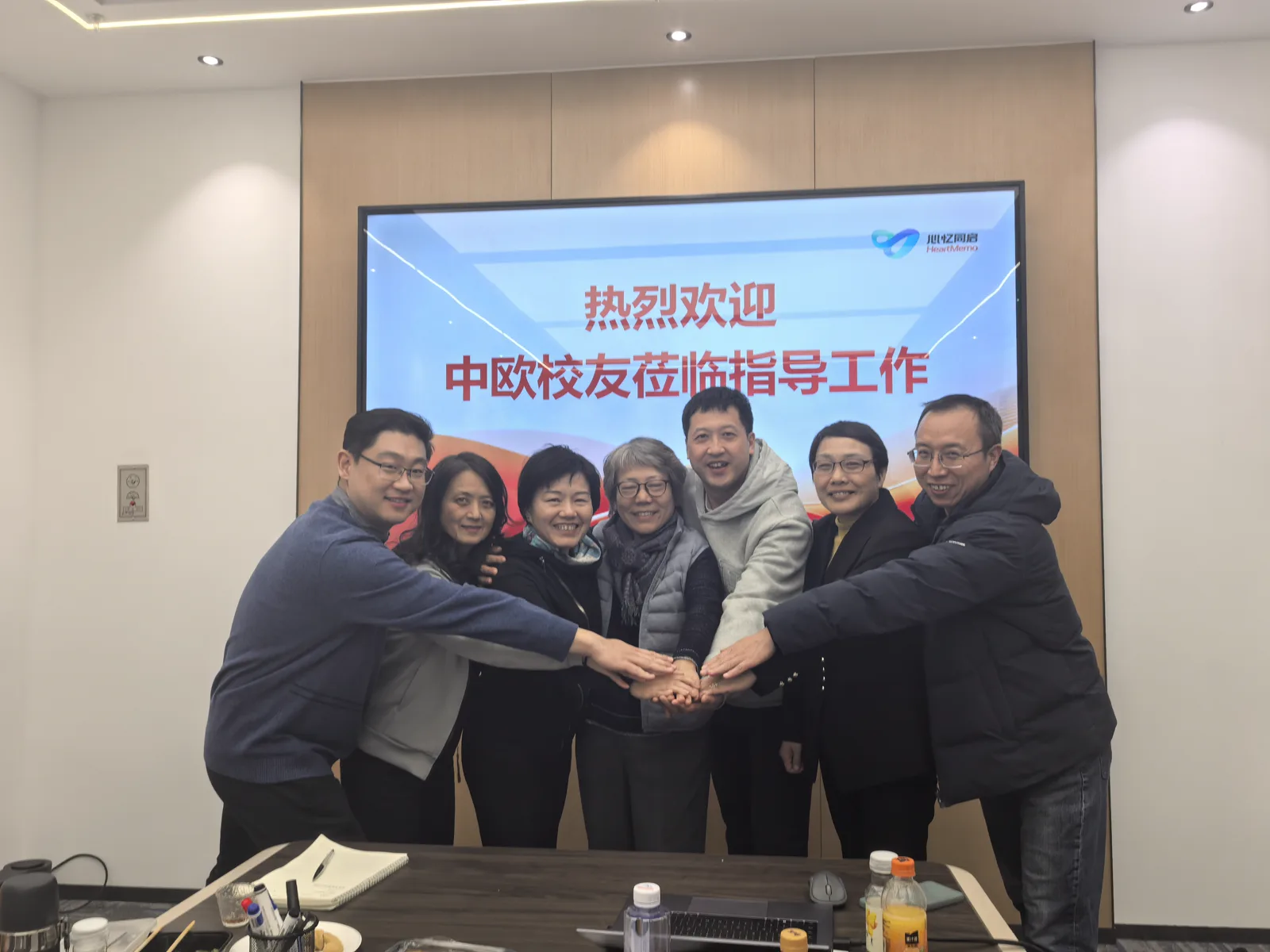 七人在欢迎中欧校友莅临指导工作的屏幕前叠手合影